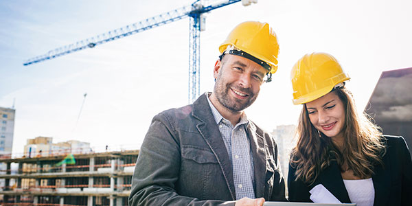 Hombre y mujer se encuentran en una construcción, vestidos como ingenieros