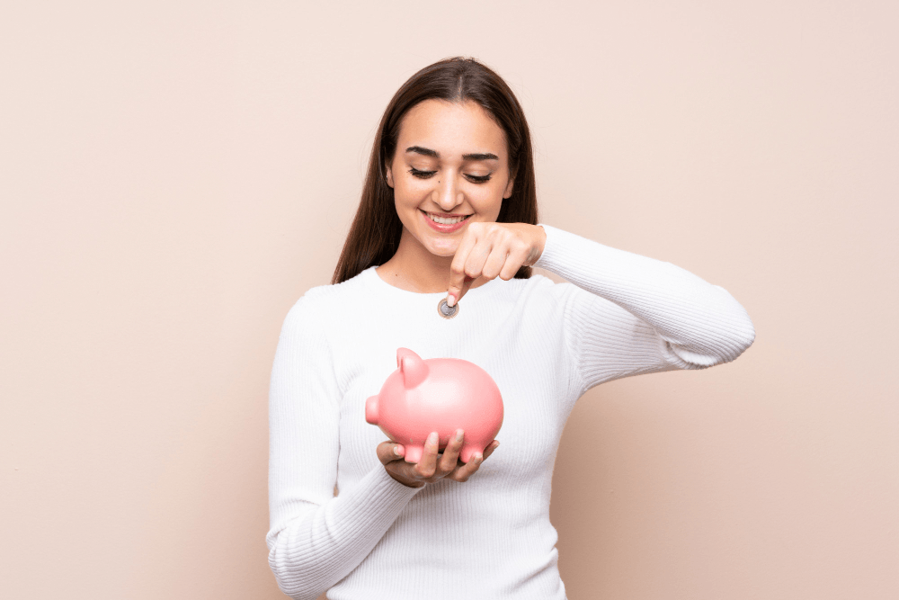 Mujer sosteniendo una alcancía mientras deposita una moneda