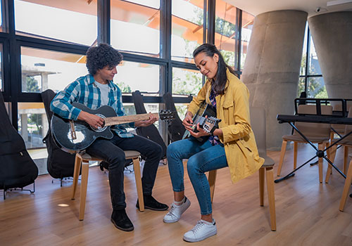 Cra 60_modelos_259 - Dos jóvenes sentados tocando guitarra, dentro de un salón de música del Centro de bienestar integral carrera 60. 