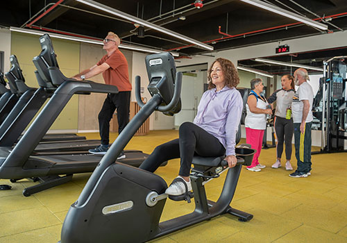 Cra 60_modelos_054 -  Personas mayores haciendo ejercicio en máquinas de cardio del gimnasio del Centro de bienestar integral carrera 60, personas mayores hablando con entrenador del gimnasio. 