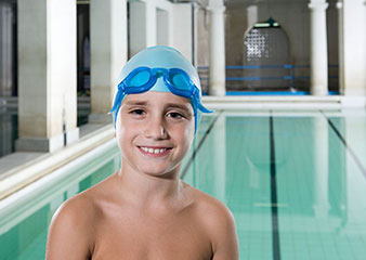Niño sonrriendo con gorro y gafas de natación, piscina de fondo