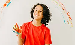 Niño sonrie en primer plano con las manos pintadas de colores
