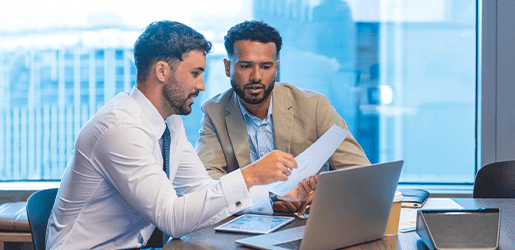Dos hombres ejecutivos revisando un document que sostienen en sus manos.