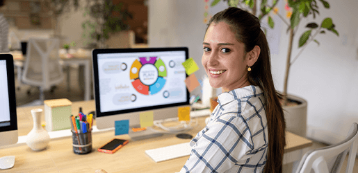 Mujer joven sonriendo, sentada frente a un escritorio con una presentación en su computador.