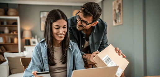 Mujer y hombre realizando una compra virtual. La mujer tiene una tarjeta de crédito en sus manos, mientras qué, el hombre sostiene una caja