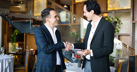 dos hombres estrechando sus manos en forma de saludo, viéndose fijamente. Uno de ellos sostiene una tablet en su mano.