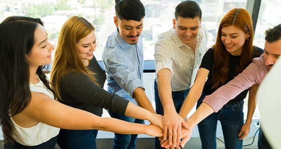 grupo de personas reunidas en medio círculo poniendo sus manos en el centro.