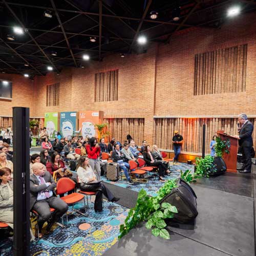 Evento de tecnología con asistentes, en el escenario una pantalla con la palabra Tech. 
