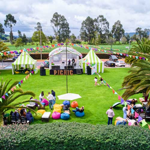 Evento al aire libre en un jardín con carpas, mesas y varias personas. 