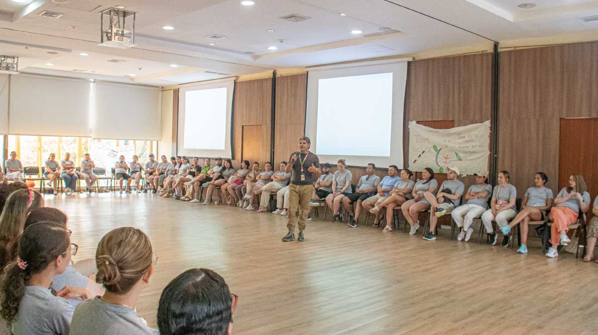 Convención empresarial con asistentes sentados en círculo en un salón amplio con una pantalla.
