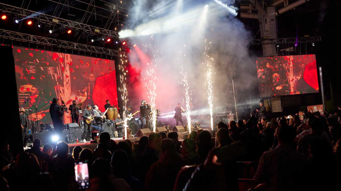  Un escenario iluminado con pantallas gigantes y público disfrutando un concierto. 