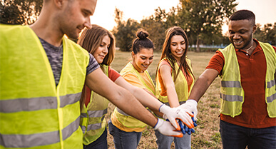 grupo de jÃ³venes mirando hacia abajo y sonriedo con sus manos extendidas hacia el centro.Â 