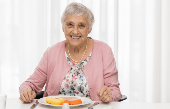 imagen de una adulta mayor sentada frente a un comedor con un plato y cubiertos.