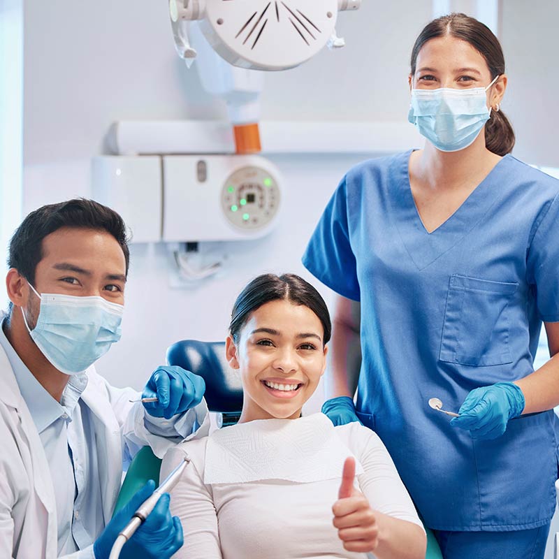Hombre odontólogo, mujer enfermera y paciente, miran a la cámara y sonríen