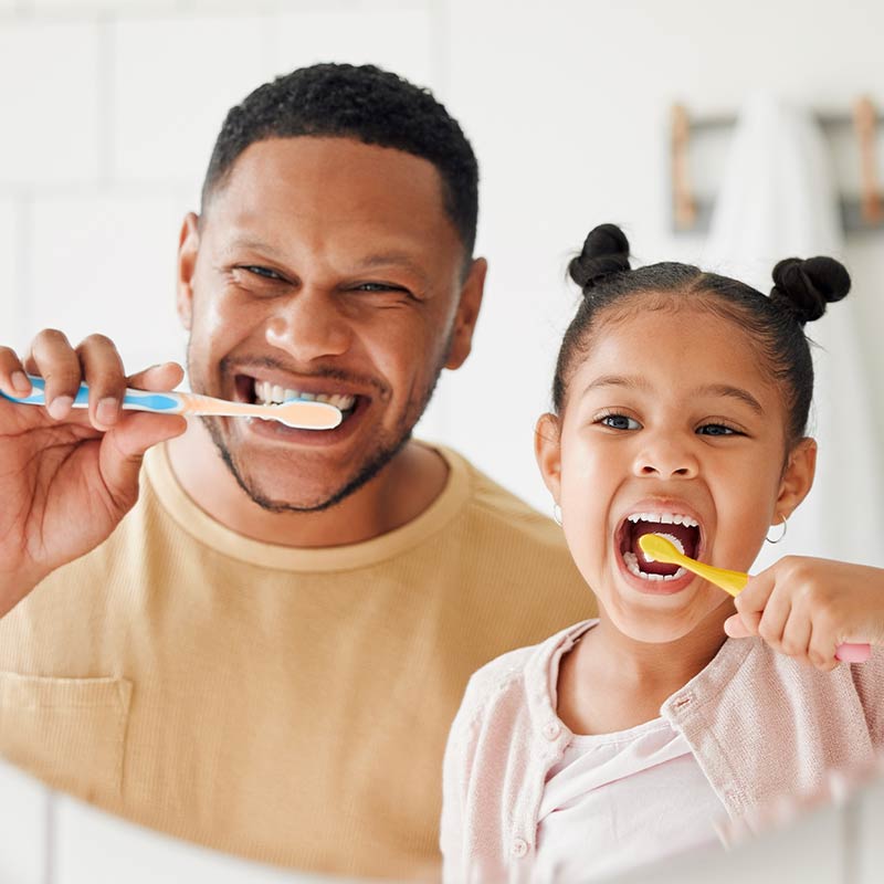 Hombre adulto y una niña se cepillan los dientes  