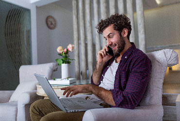 Hombre llamando por celular mientras mira su laptop