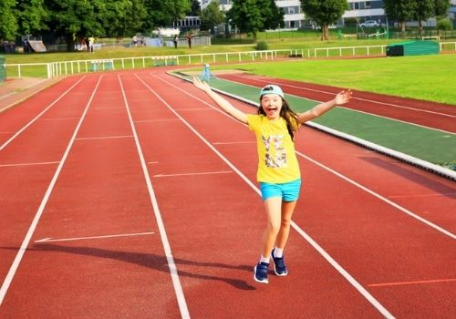 ninña con sindrome de Down feliz corriendo en una pista de atletísmo